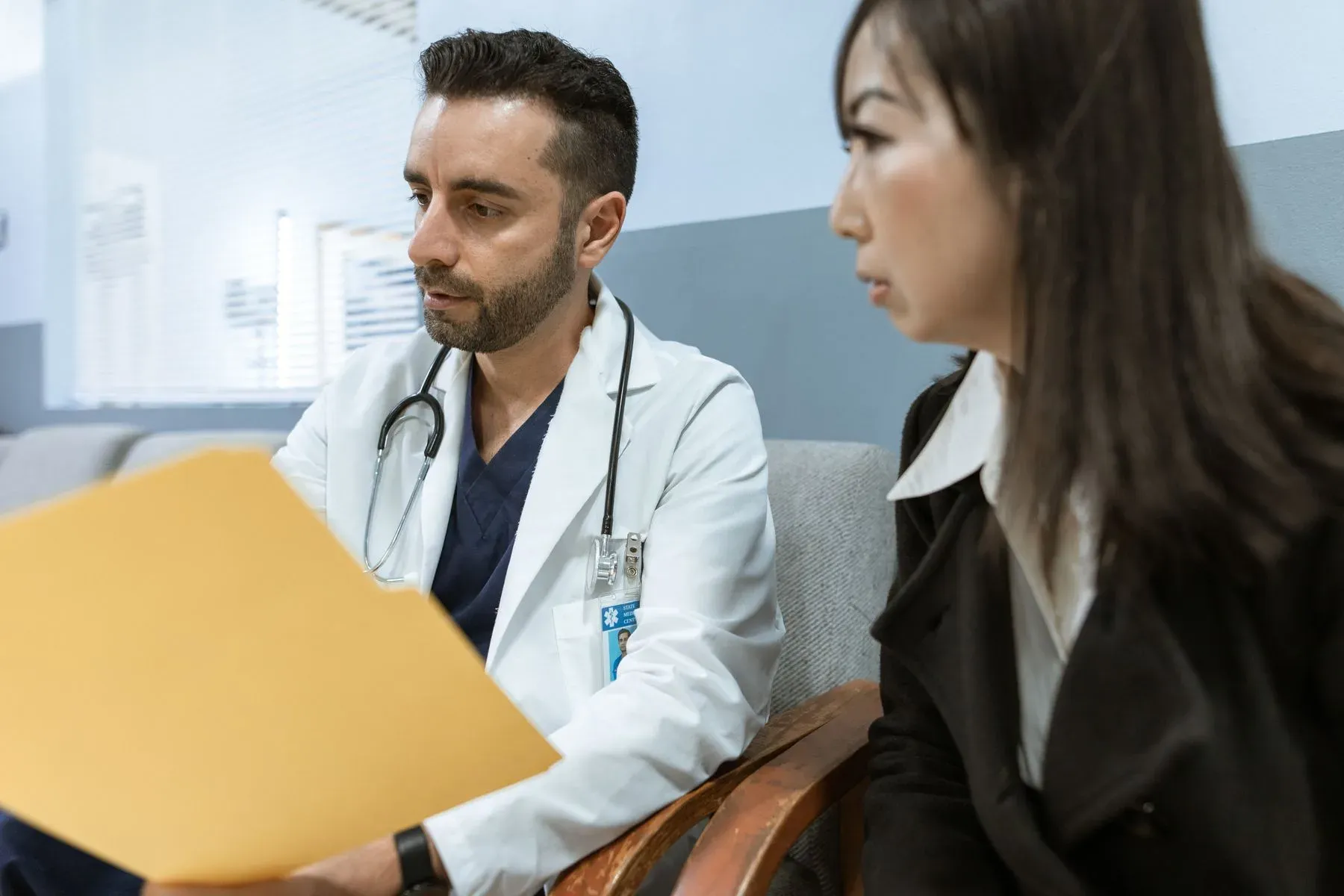 A physician in a white coat going through a patient's records with her at a desk