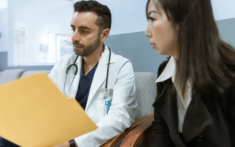 A physician in a white coat going through a patient's records with her at a desk