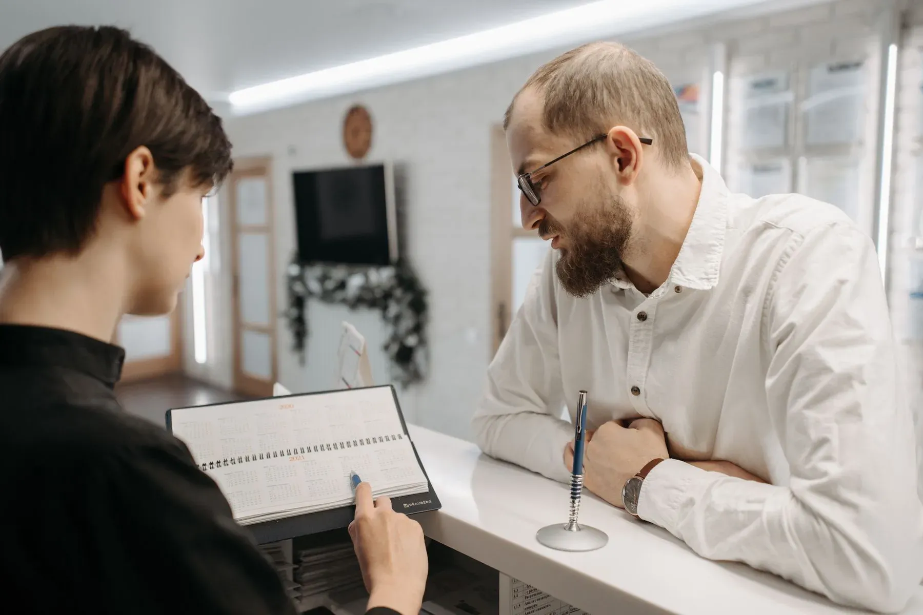 A receptionist and a patient going over an appointment book at a clinic front desk